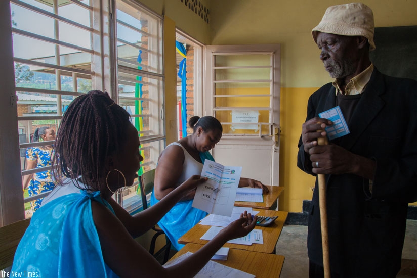 A polling agent at La Colombiere polling station guides an elderly man on the voting procedures. Voter turn-up was 98.3%. (Faustin Niyigena)