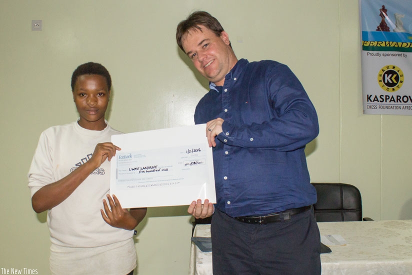 Graham Jurgensen presents Eagles Chess Club (ECC) youngster, Sandrine Uwase, 13, with a 500 USD dummy check after the P.4 student of E.P Karugira was announced 2016 winner of the KCF-A academic study grant. KCF-A awards annual academic study grants to deserving members of the African chess community. (James Karuhanga)rn