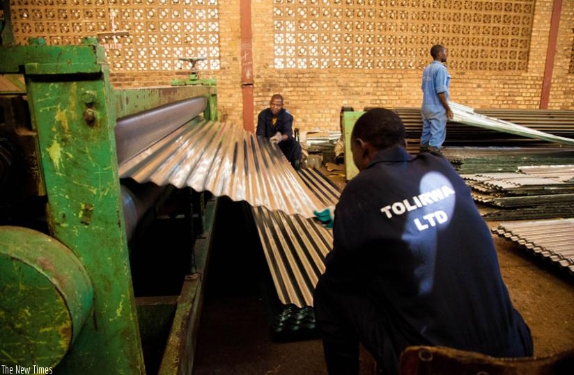 Workers of Tolirwa Industries pull ready-to-be-sold iron sheets from a machine. (File)