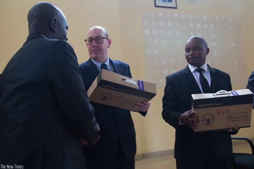 Ted Maly, the Unicef country representative (C) hands over a laptop to Jean Damascene Usabyimana, the Sector Education Officer for Gahanga in Kicukiro District (L), as the Minister for Primary and Secondary Education, Olivier Rwamukwaya, looks on yesterday. (Timothy Kisambira)