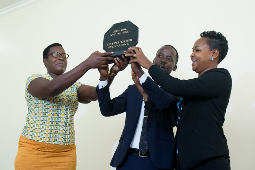 Kamonyi vice mayor in charge of social affairs Prisca Uwamahoro (L) and  the National Youth Council coordinator for Kamonyi, Ernest Kamanzi, (C) receive the district's award for to....