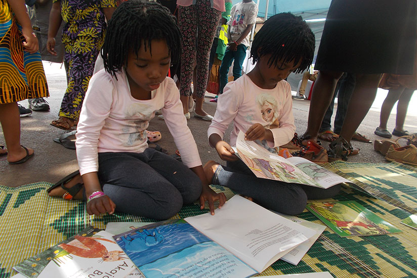 Children read storybooks at the Kigali car-fee zone during a recent exhibition by local publishers. / Elias Hakizimana