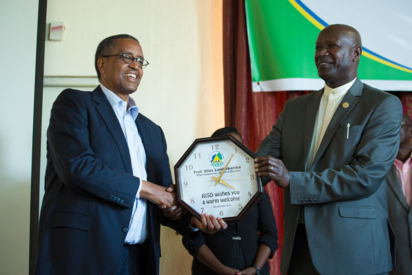 Prof. Silas Lwakabamba (L), who was installed as the new RISD board chair during the launch of the app, receives a gift from his predecessor Bishop Nathan Gasatura. / Timothy Kisambira