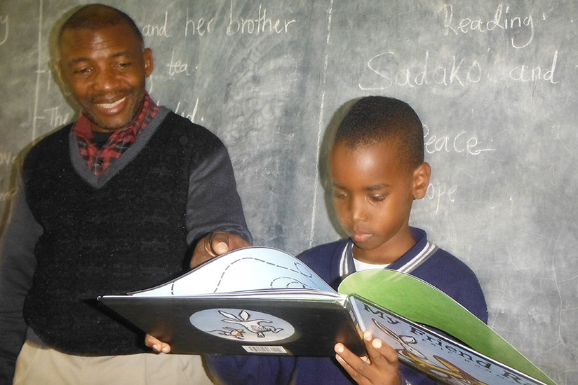 A pupil reads a book with the guidance of his teacher. / Dennis Agaba