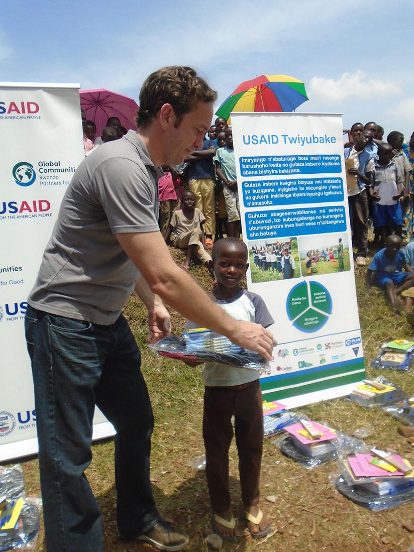 Marc Valentin, the Director of Programme Management at USAID Twiyubake, hands over scholastic materials to one of the children. / Steven Muvunyi