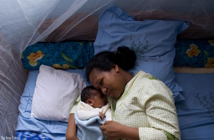 A nursing mother sleeps under a mosquito bed net with her baby. / File