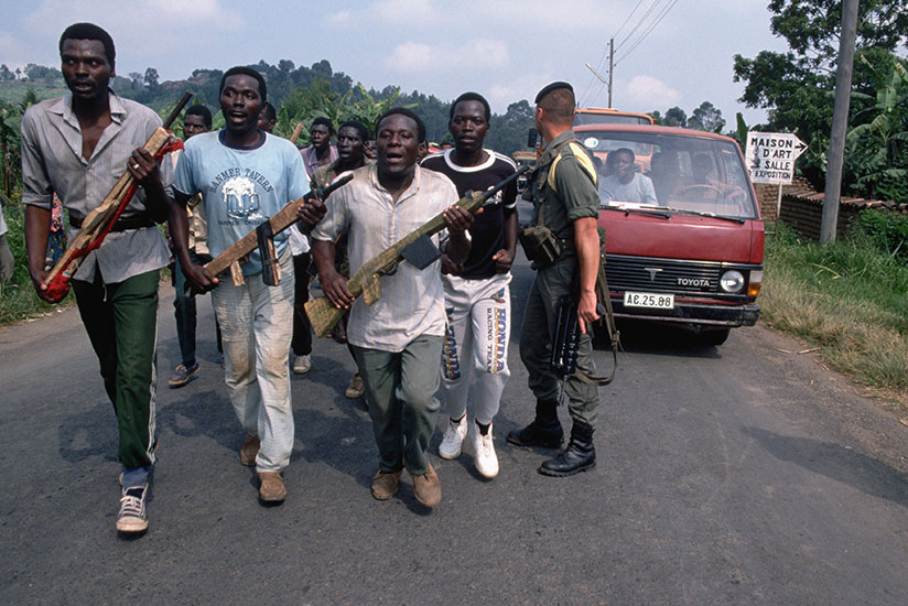 A group of 'Interahamawe' recruits carrying model rifles march down a road as a French soldier looks on. / Internet photo