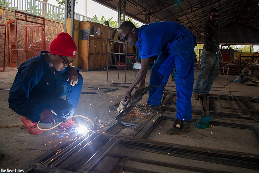 Kabagambe and one of his employees welding a door frame at the workshop. He also makes metallic windows, ventilators, and beds, among other products. / Timothy Kisambira.  