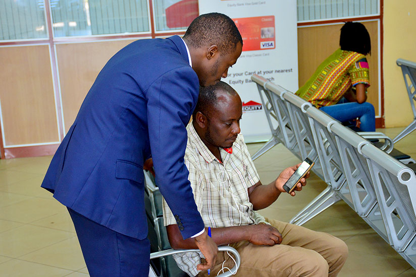 Bank staff helps a customer to set up a mobile banking service on his phone. / Lydia Atieno