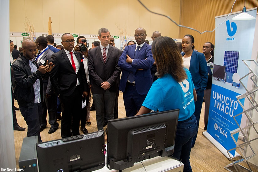 Solar Company BBOXX's agent explains to Minister Musoni (hands folded) and other guests what the company does at an exhibition during the conference. Faustin Niyigena.