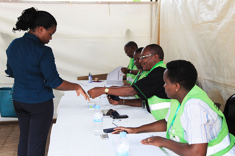Volunteers check the passport of one voter before casting her vote in Kigali