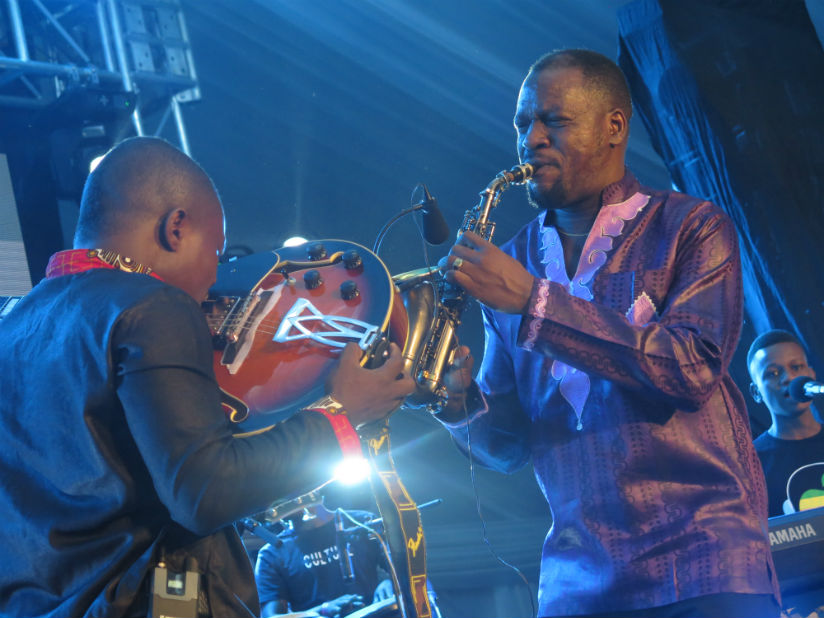 Katumwa (right) plays a saxophone as his band member shows skills playing a guitar with his teeth. / Eddie Nsabimana