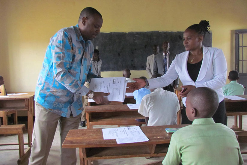 State Minister for Primary and Secondary Education, Isaac Munyakazi (L) distributes exams to candidates at GS Nyagatare on day one of PLEs (Courtesy)