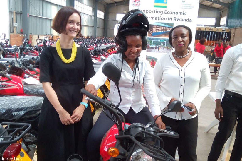 One of the land officers tries out a motorcycle as Mukamana (right) and DFIDu2019s Metcalf (left) look on during the handover ceremony at Bollore Warehouse at the Special Ezonomi....