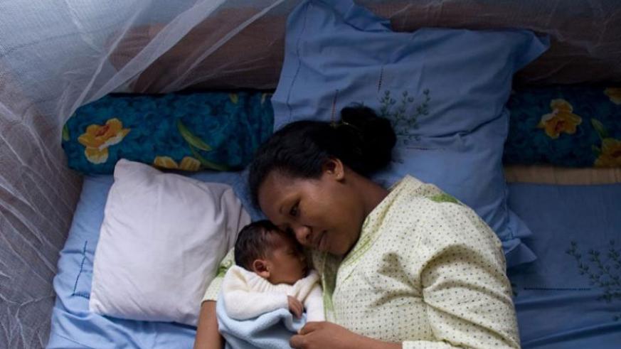 A nursing mother sleeps under a mosquito bed net with her baby. / File