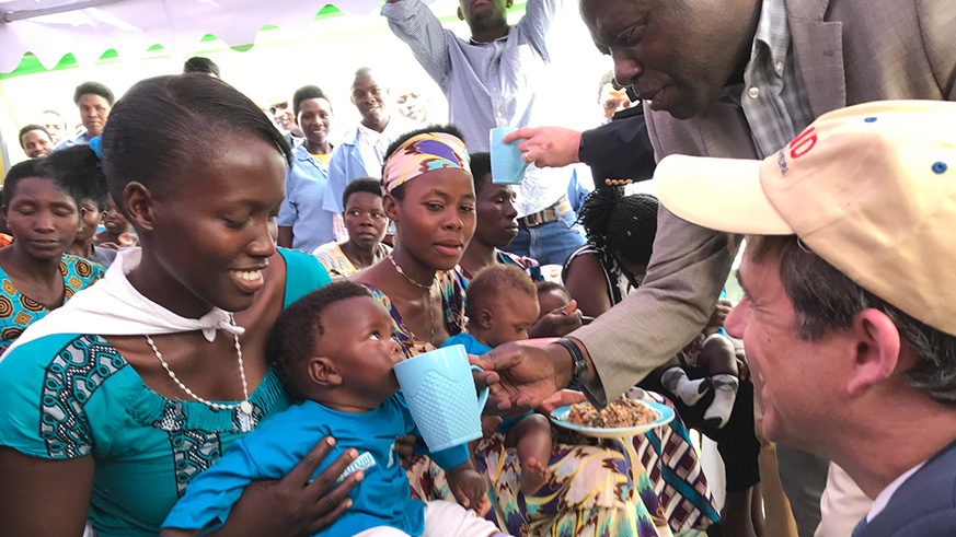 State Minister for Agriculture, Fulgence Nsengiyumva feeds a child with milk as United States Ambassador to Rwanda, Peter H. Vrooman, looks on with a smile in Bugesera during the project launch on Thursday. Courtesy.
