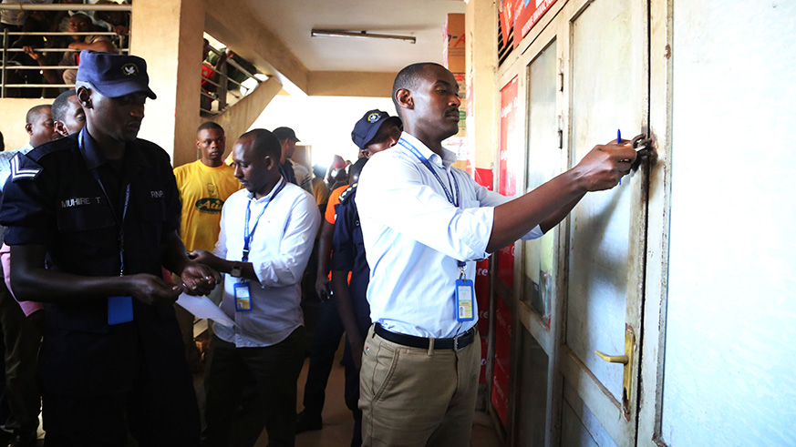 Vianney Butera, the EBM Field Operations Manager at Rwanda Revenue Authority (right), puts a padlock on the door of a shop in Nyarugenge District, Kigali yesterday as RRA started a countrywide operation to curb misuse of Electronic Billing Machines (EBMs).  Sam Ngendahimana.