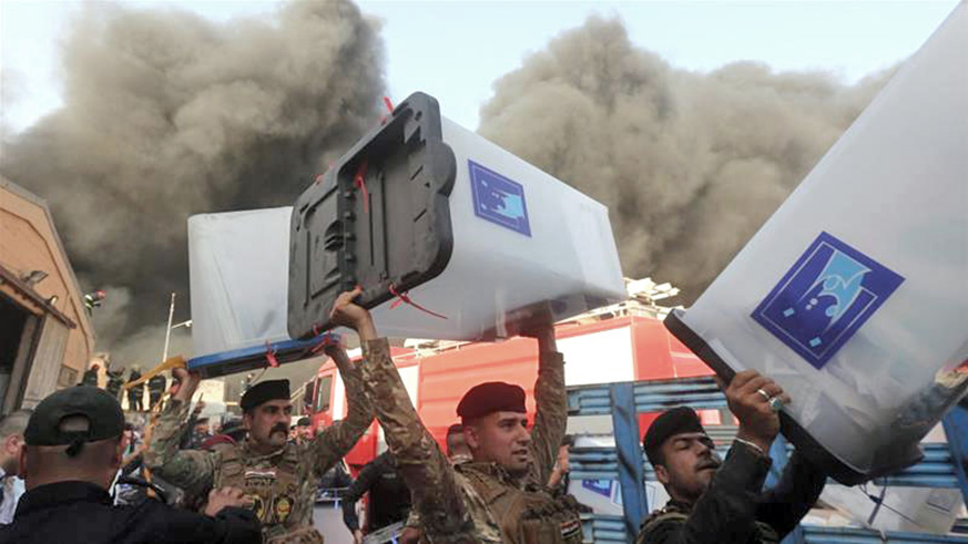 Security forces carry ballot boxes as smoke rises from the storage site in Baghdad. Net photo.