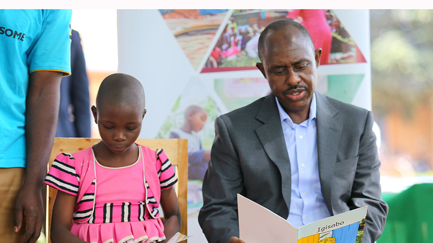Minister Mutimura reads a Kinyarwanda book with one of the children.