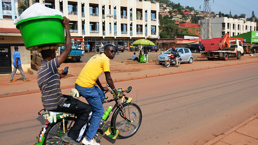 THROUGH OUR LENS: A passenger looks through his phone while carrying luggage on his head on a bicycle on the Kigali-Gatuna hihgway in Gatsata. Sam Ngendahimana. 