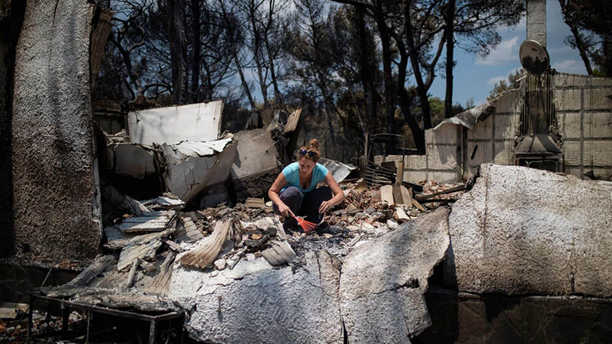 A woman tries to find her belongings underneath the debris of her burnt house following a wildfire at the village of Neos Voutzas, near Athens. Net photo.
