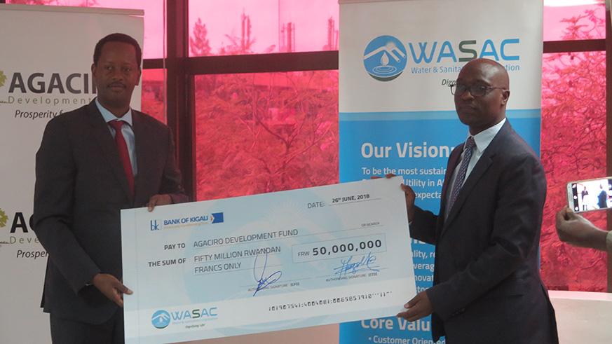 Agaciro Development Fund CEO Jack Kayonga receives a cheque Rwf50m from the CEO of Water and Sanitation Company, Aime Muzola from staff contributions to the Fund in June this year. File