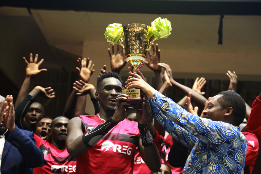 REG volleyball club captain Christophe Mukunzi receives the trophy from Anastase Shyaka, the Minister of Local Government,  as teammates in the background celebrated their historic triumph after beating Gisagara at Petit Stade on Saturday. / Sam Ngendahimana