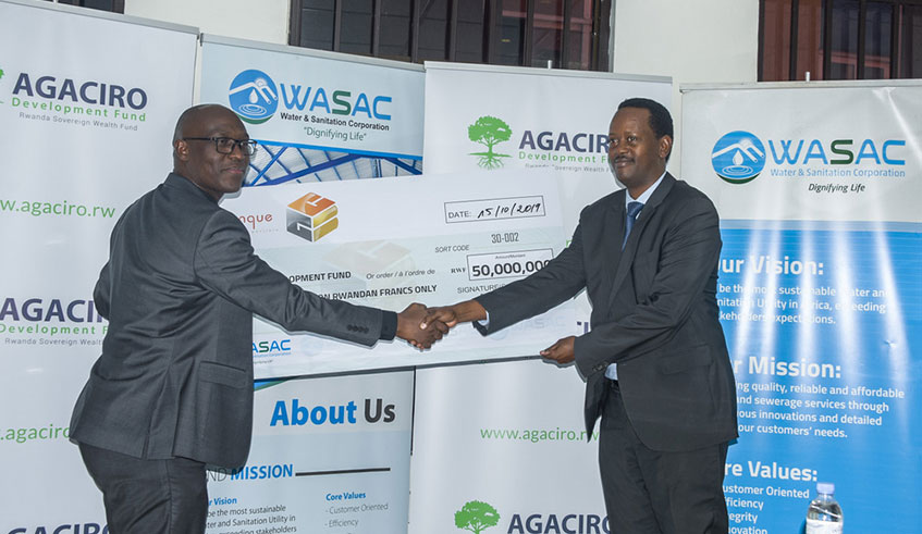 WASAC chief executive Aimu00e9 Muzola (left) hands over a dummy cheque to Jack Kayonga, the chief executive of Agaciro Development Fund in Kigali yesterday. Net photo.