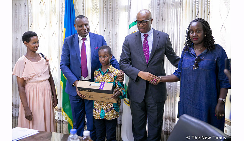 Elvin Humura, from Wisdom School, who emerged the best overall performer with aggregate 5 in the 2019 Primary Leaving Examinations, is congratulated and handed a Positivo laptop by Isaac Munyakazi, the Minister of State in charge of Primary and Secondary Education, as Samuel Mulindwa, the Permanent Secretary in the Ministry of Education, and Humurau2019s mother Leah Mukayuhi (left) and aunt (right) at the Ministry of Education in Kigali on December 30, 2019. Photo 