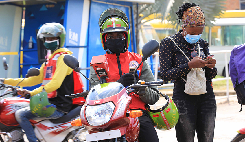 A taxi moto client does mobile money transactions to pay a motorist to curb the spread of Covid-19. / Craish Bahizi.