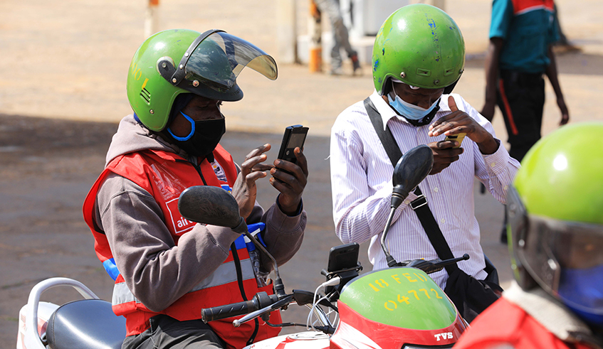 A taxi moto operator and his client do mobile money transaction to pay the transport fee. The new guidelines encourage passengers  to use cashless payments. / File.