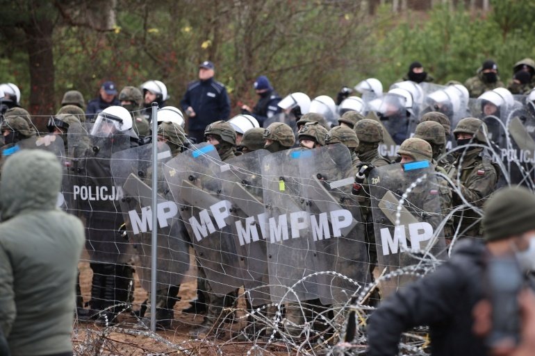 Polish law enforcement officers and frontier guards stand next to a barbed wire fence as hundreds of migrants gather on the Belarusian-Polish border in an attempt to cross it in the Grodno region, Belarus. 
