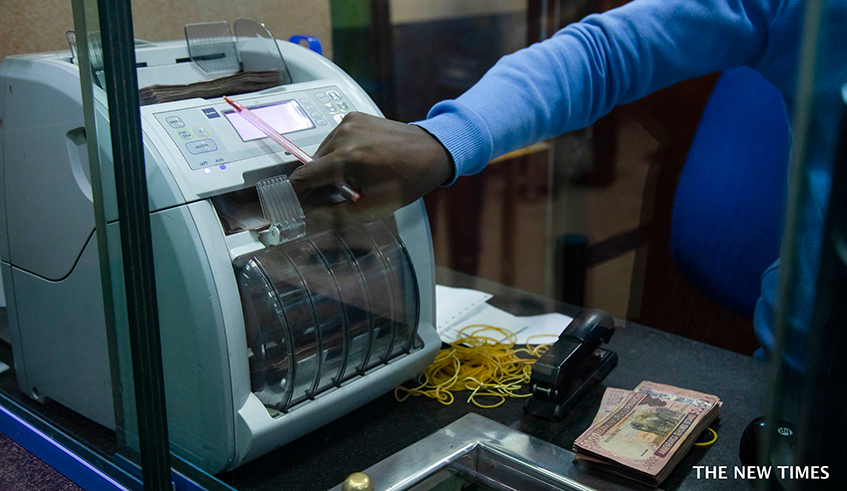 A bank teller counts money as he serves a customer at Bank of Kigali headquarters. / Photo: File.