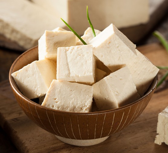 Tofu is prepared by thickening soy milk and then pressing the resulting curds into solid white blocks of varying softness. 