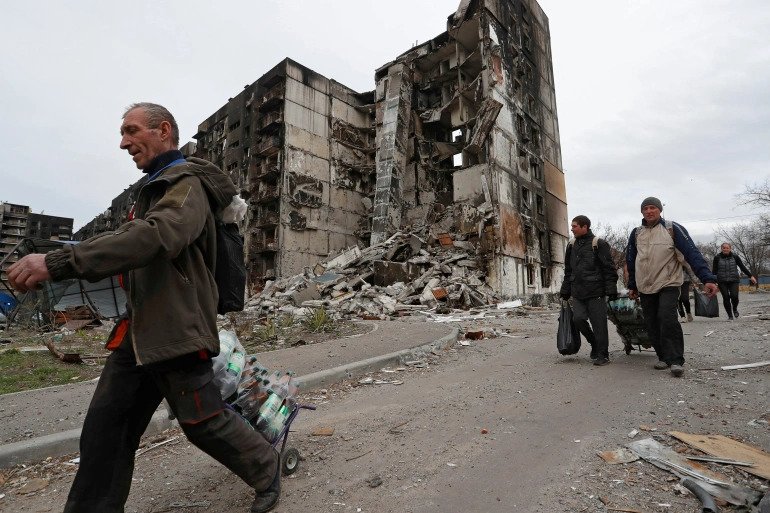 Local residents walk past a building destroyed during Ukraine-Russia conflict in the southern port city of Mariupol. 